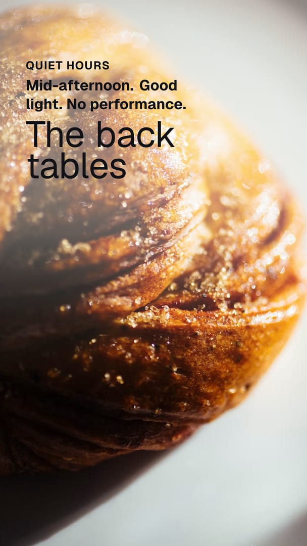 Ad for a coffee shop: a very close photograph of a twisted pastry bun crusted with coarse sugar, on a pale plate in bright light. The words on the picture read Quiet hours, Mid-afternoon. Good light. No performance, The back tables.